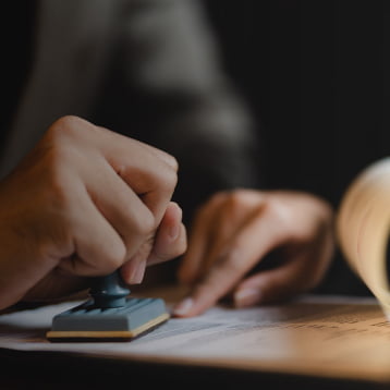 A hand stamps an iGaming compliance document on a dark surface, with a blurred rolled paper in the background.